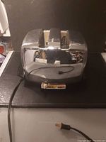 Front view of a shiny chrome toaster with two bread slots and a black base on a dark surface.