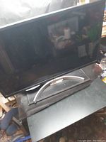 Front view of black computer monitor with curved silver stand base on black table.