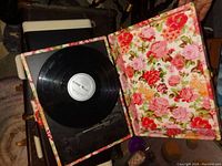 Open floral patterned luggage case revealing a black vinyl record on turntable