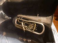 Silver tuba in black carrying case with three valves and visible wear.