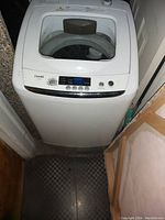 Front view of a white Panda compact portable top-load washing machine with lid open, digital display and controls visible on front panel.