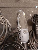 Gray Dremel rotary tool with power cord, textured grip, and small accessory bits.