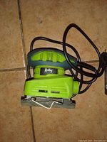 Green Relay orbital sander power tool lying on a tiled floor showing power cord and sanding base