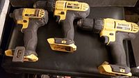Photo showing three yellow and black DeWalt cordless power drivers. Each tool is marked 20V Max. No batteries or chargers are present. Tools include two drill drivers and one impact driver.