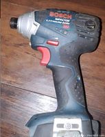 Bosch cordless impact driver with 18V Lithium-Ion branding resting on a wood floor.