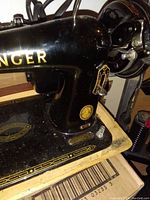Close-up side view of the black Singer sewing machine showing gold Singer logo, gold decorative detailing on the base, and round gold medallion.