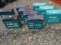 Overview of 12 electric scooter batteries in outdoor setting, showing green and blue casings with terminal covers and visible branding.