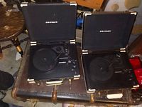 Two Crosley portable record players opened to show turntables, tone arms, and branded lids, resting on a table.