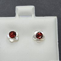 Pair of 10k gold stud earrings with red garnet stones set in mother of pearl floral shaped settings shown on a white textured display card.