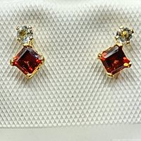 Close-up front view of 10kt yellow gold garnet and diamond stud earrings on white textured display.
