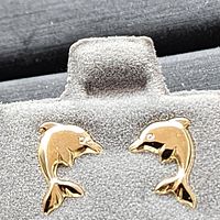 Pair of 14k yellow gold dolphin-shaped earrings displayed on a grey earring holder. Each earring shows smooth and polished dolphin detail.