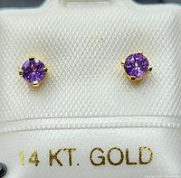 Pair of round amethyst stud earrings set in 14k yellow gold on white display labeled 14 KT. GOLD.