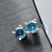 Front view of both blue diamond stud earrings on black surface.