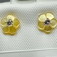 Close-up front view of both 14kt yellow gold flower-shaped stud earrings with diamond centers held on a white display card.