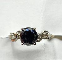Straight-on view of ring showing round black center diamond and side stones