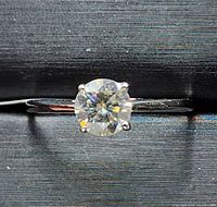 Close-up photo showing 10k gold ring with round moissanite gemstone set in 4 prong solitaire setting.