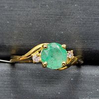 Top-down view of ring showing round green emerald center and flanking diamonds