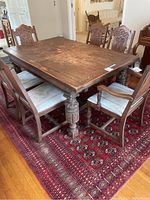 Full view of antique solid wood dining table with six matching chairs set on patterned red area rug in dining room.