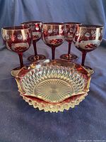 Five ruby cut wine glasses and one ruby diamond point candy dish shown together on a blue cloth background.