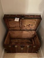 Front angled view of an open antique wooden steamer trunk showing interior wooden panels and hinged lid.