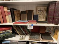 Shelf with a mix of vintage and antique books including various titles by Ralph Waldo Emerson and other works, some leatherbound and cloth hardcover.