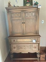 Front view of vintage oak cupboard cabinet showing detailed carved upper doors, drawer, and lower doors with round wood knobs.