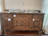 Front view of antique wood sideboard displaying ornate carved details, decorative knobs, and top surface with glassware (not included)