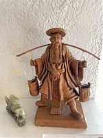Front view of brown detailed figurine of an Asian man with carrying pole and buckets, and green horse figurine beside him.
