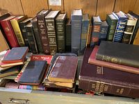 Multiple hardcover and softcover Bibles and prayer books arranged upright and stacking, showing titles and condition.