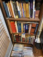 Three wooden shelves holding mostly hardcover books with visible titles on religion, finance, and health. Below shelves are two boxes filled with folded maps.