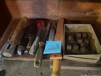 Overview of knives, cutting tools with wooden handles, leather sheaths, and box of wooden stamps.