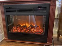 Front view of electric fireplace showing glowing flame and log effects within wooden Amish-style mantle.