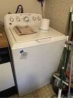 Front view of GE top load washer showing control panel, top lid, included user manual, and accessory part on top.