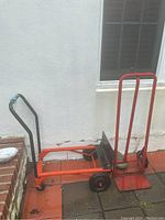 Orange hand truck can convert between upright dolly and laying down flat cart configuration. Black handles, black rubber wheels, foldable base plate.