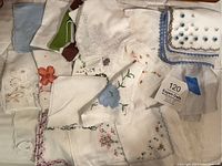 Handkerchiefs spread out showing variety of floral embroidery, scalloped, and lace edges