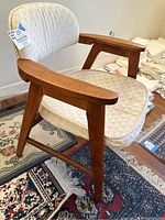 Profile view of midcentury modern wooden chair with cream custom cushions showing angled legs and wide armrest detail.