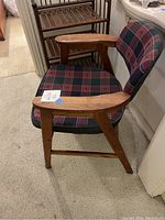 Front perspective of plaid upholstered wooden armchair positioned next to wooden rack