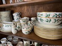 Shelved collection of place settings, cups, saucers, creamer, sugar bowl, gravy boat, serving bowls, charger plates