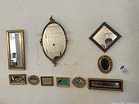 Overall view of all 11 mirrors mounted on a white wall in varying sizes and styles including gold and blue frames