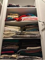 Shelves holding multiple folded fabrics in assorted colors and patterns such as stripes, plaids, solids.