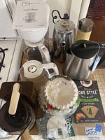 Full lot showing Sunbeam percolator, Mainstays coffee maker, Oster electric kettle, Hamilton Beach mini drip coffee maker, Braun coffee grinder, and assorted coffee filters.