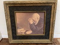 Front view of vintage framed print showing elderly man praying at dinner table with bread, bowl, and open book.