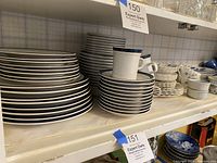 Shelf showing multiple stacks of blue rimmed plates, white plates, and cups and saucers typical of vintage dinnerware sets.