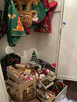 Overview of large collection of vintage Christmas decorations including ornaments in boxes, holiday fabric decor hanging above, and a silver deer figurine on the side.