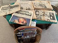 Photo showing an assortment of vintage newspapers laid out over a table and a basket containing magazines and booklets on American history.