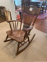 Front angle view of the vintage wooden rocking chair with leather embossed seat and carved backrest.