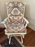 Front view of vintage white rocking chair with custom patterned cushions showing floral and geometric fabric.