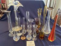 Group of 15 vintage art glass vases arranged showing variety in color, design, height and shape on dark fabric background.