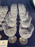 Photo showing the 12 goblets and 11 wine glasses with floral etching arranged in rows with dark cloth background