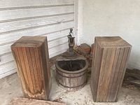 Wide view showing two tall vintage wood plant stands flanking a vintage water pump mounted in a circular wood barrel base.